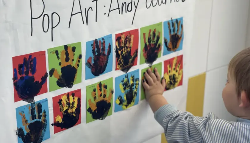 Manos pequeñas crean arte pop inspirado en Andy Warhol. Un niño toca una obra colorida, celebrando la creatividad infantil.