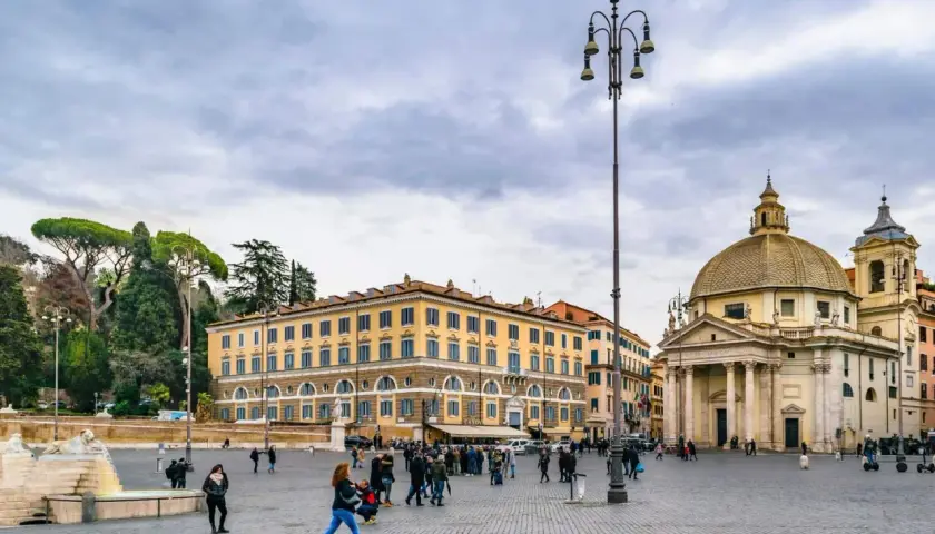 Piazza del Popolo a Roma a novembre, con la chiesa gemella e il palazzo giallo sotto un cielo nuvoloso.