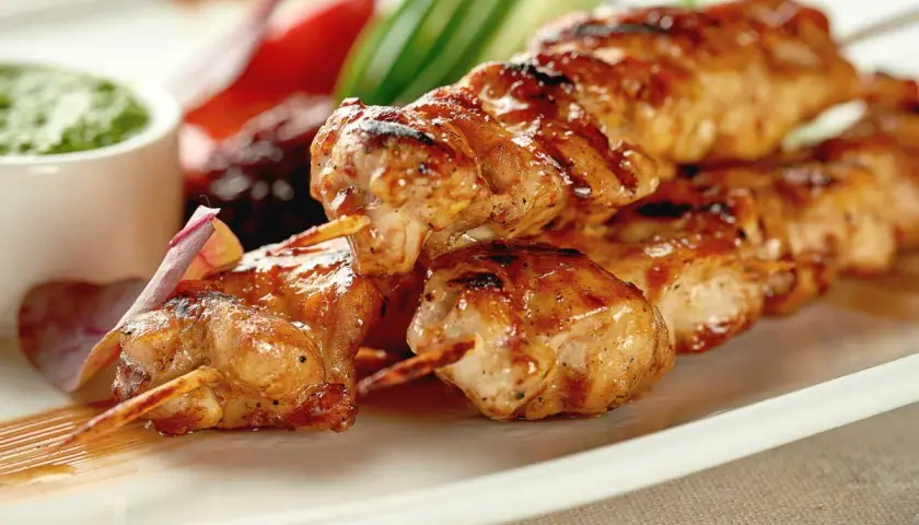 Délicieuse brochette de poulet grillée, servie avec une sauce verte et des légumes croquants. Un plat savoureux et coloré.