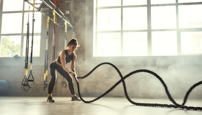 Kobieta ćwiczy z linami treningowymi, pokazując, crossfit co to za intensywny trening.