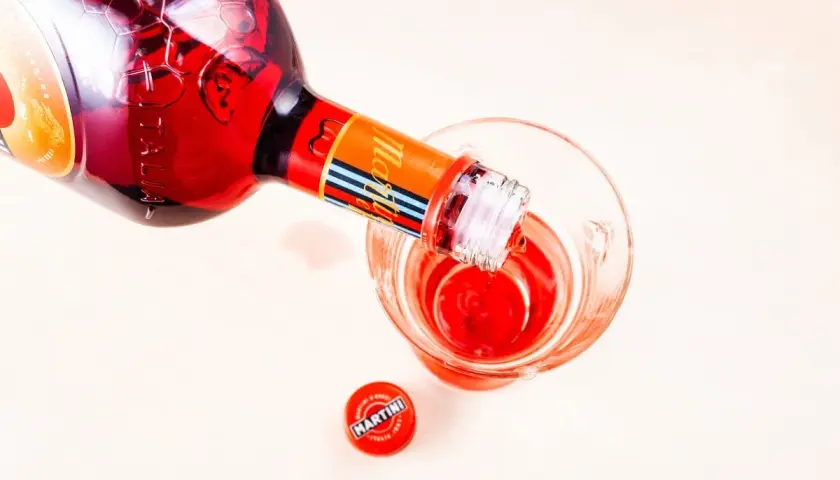 Czerwony Martini Fiero Tonic nalewany do szklanki. Obok leży czerwona zakrętka z logo Martini.