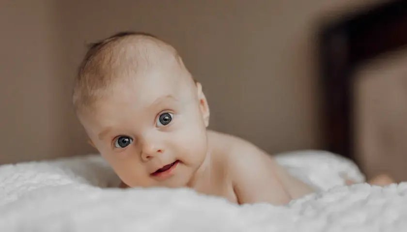 Niemowlę na brzuchu, z zaciekawieniem patrzące w obiektyw. Jego oczy, choć mogą sugerować zez u niemowlaka, są po prostu skupione na otoczeniu.