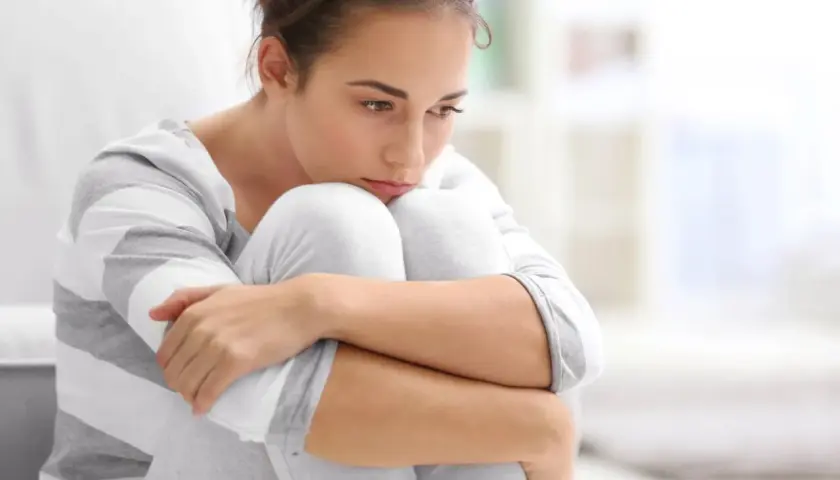 Ragazza con sguardo pensieroso, abbracciata alle ginocchia, simbolo di ansia ad alto funzionamento.