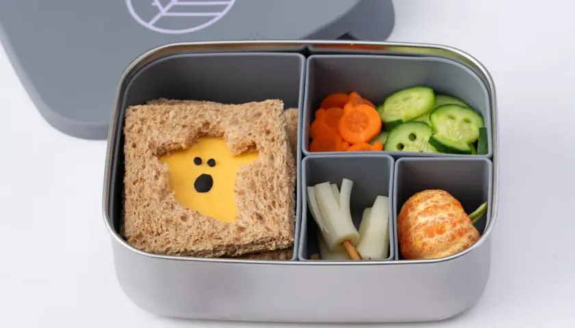A spooky Halloween bento box with a ghost-shaped cheese sandwich, carrot slices, cucumber rounds, and a peeled tangerine.