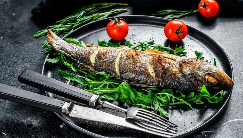 Poisson entier au barbecue, servi sur un lit de roquette avec des tomates cerises et des herbes.