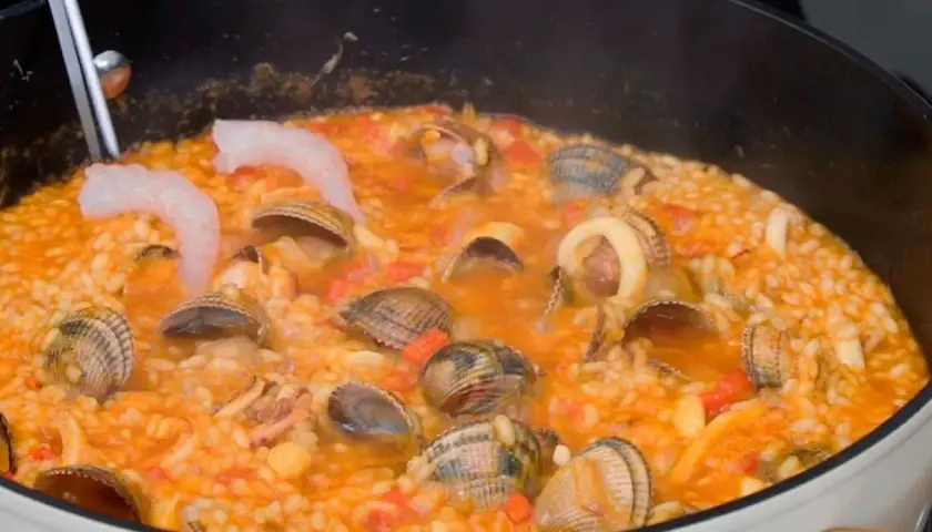 Un delicioso arroz a la marinera burbujea en una sartén, con gambas, almejas y calamares.
