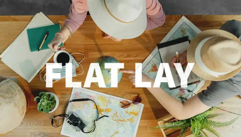Widok z góry na stół z mapami, globusem, aparatem i notatkami. Dwie osoby planują podróż, tworząc inspirujący **flat lay**.