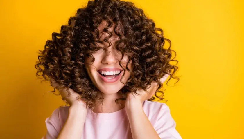 Mujer sonríe con cabello rizado y voluminoso. Descubre cómo hidratar el cabello después de una permanente para mantenerlo así de saludable.