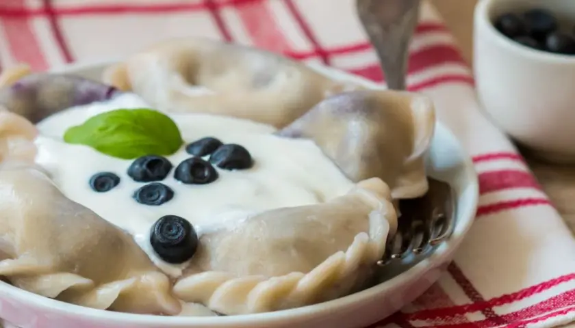 Pyszne pierogi z borówkami amerykańskimi, polane śmietaną i ozdobione świeżymi owocami. Idealne na letni deser.