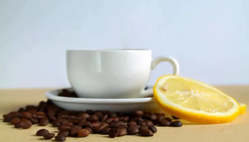 Tazzina di caffè con chicchi sparsi e una fetta di limone, un contrasto di sapori per iniziare la giornata.