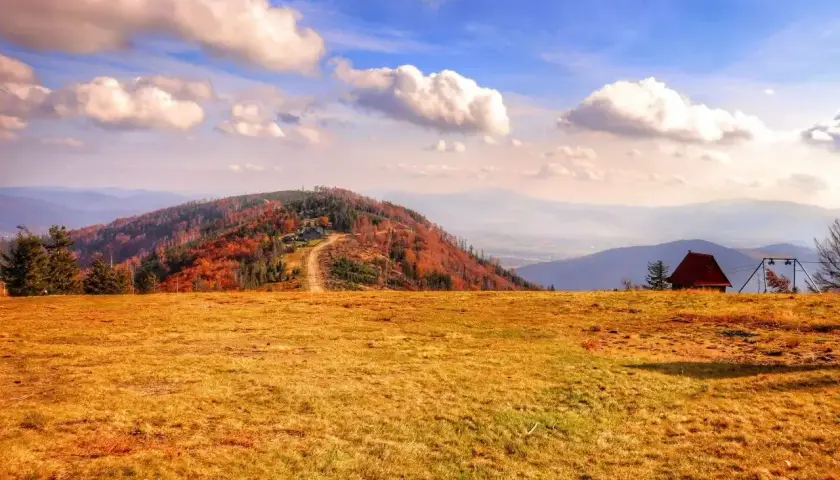 Jesienne barwy gór w Szczyrku. Złociste łąki, kolorowe drzewa na zboczu i malownicze pasma górskie w oddali.