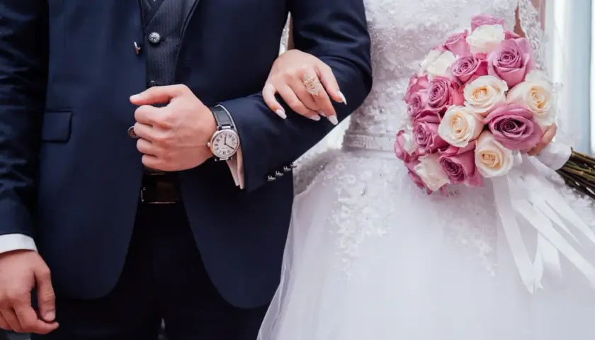 Un couple uni, main dans la main, bouquet de roses roses et blanches. Vive les mariés !