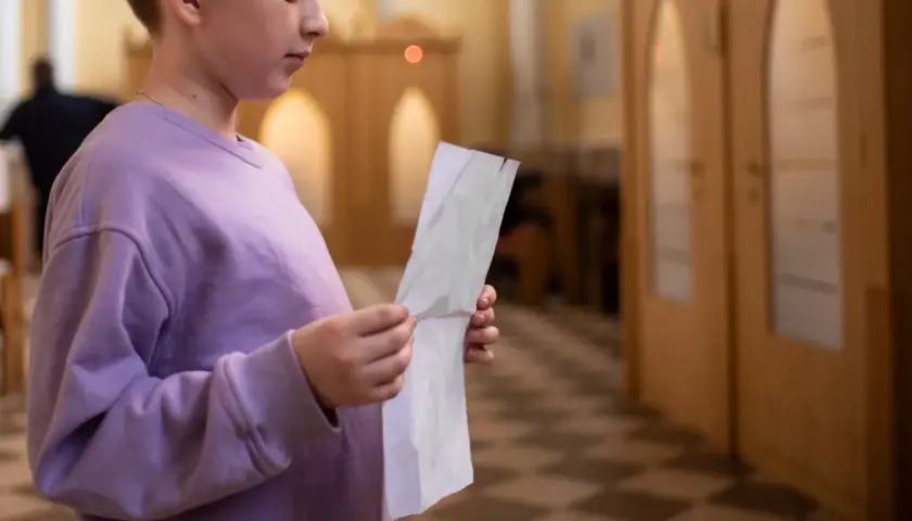 Młoda osoba w fioletowej bluzie trzyma kartkę, przygotowując się do spowiedzi świętej w kościele.