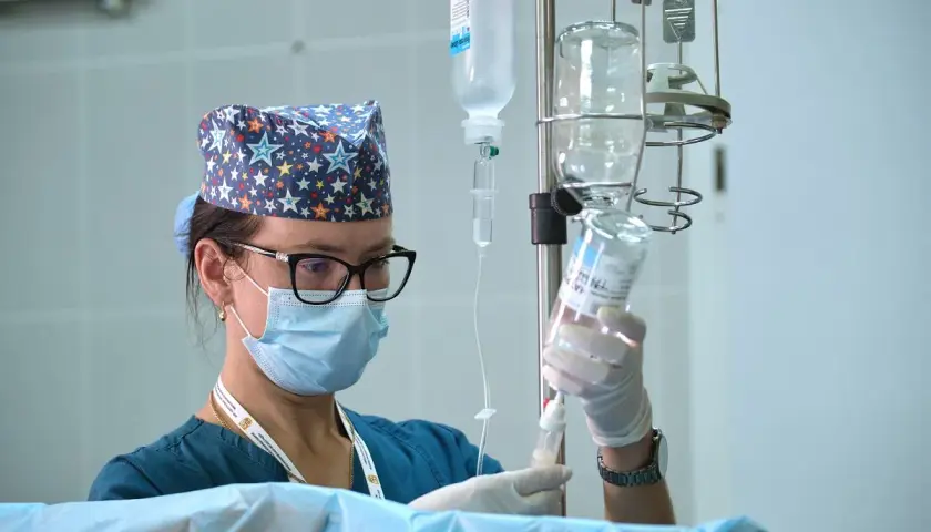 Pielęgniarka oddziałowa w maseczce i czepku z gwiazdkami przygotowuje kroplówkę. Ciekawe, ile zarabia pielęgniarka oddziałowa za taką odpowiedzialną pracę.
