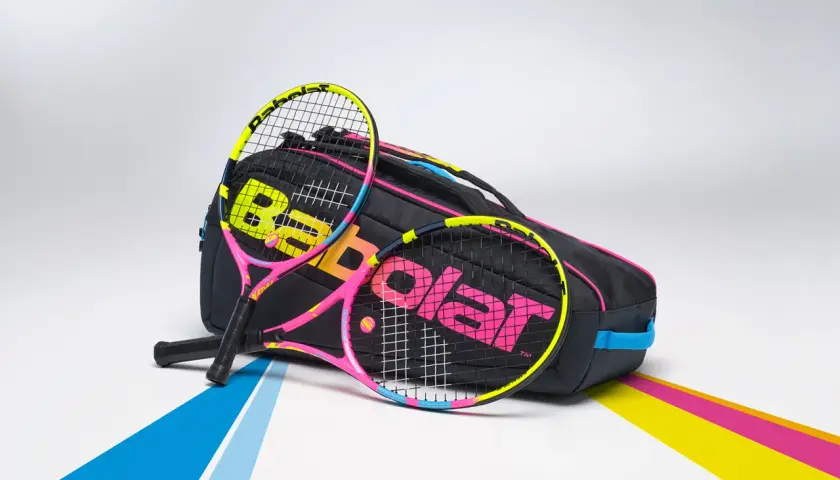 Dwie kolorowe rakiety tenisowe, jakich używałby Rafael Nadal, leżą obok czarnej torby z logo Babolat.