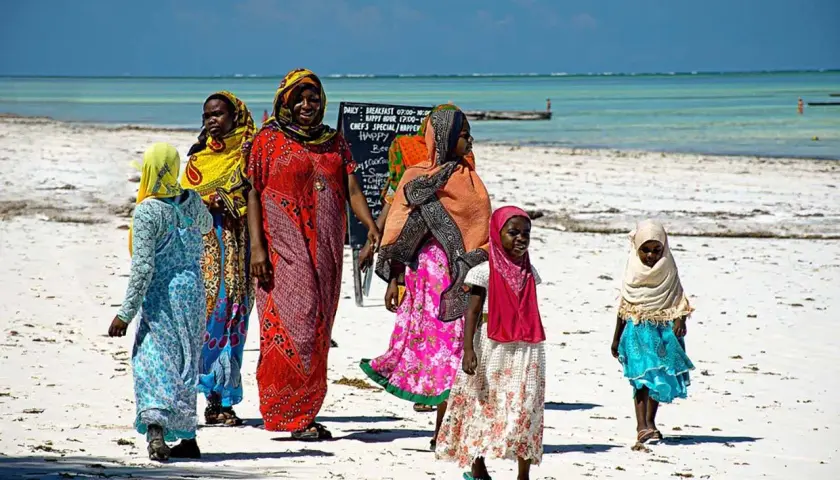 Zanzibar ludność w kolorowych strojach spaceruje po piaszczystej plaży. Dzieci i kobiety cieszą się słońcem i widokiem oceanu.