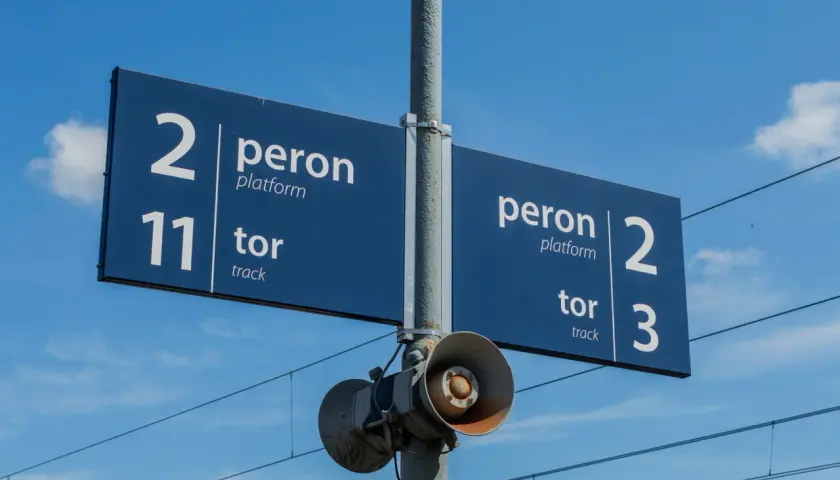 Niebieskie tablice informacyjne na słupie wskazują numery linii kolejowych: peron 2, tor 11 oraz peron 2, tor 3.