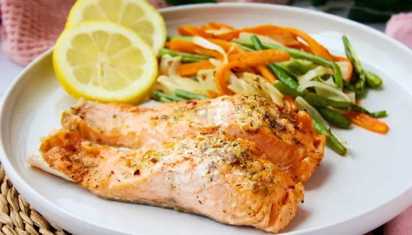 Dos filetes de salmón al microondas con verduras salteadas y rodajas de limón.