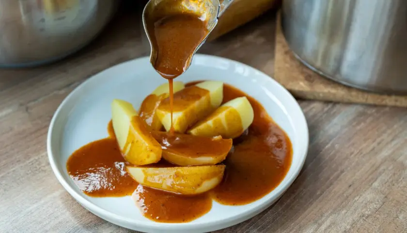 Eine Schöpfkelle gießt eine köstliche braune Sauce über Kartoffelspalten auf einem Teller.
