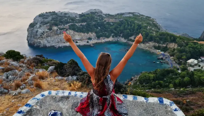 Widok na zatokę Anthony Quinn na Rodos. Kobieta z rękami w górze podziwia jeden z najpiękniejszych miejsc na wyspie.