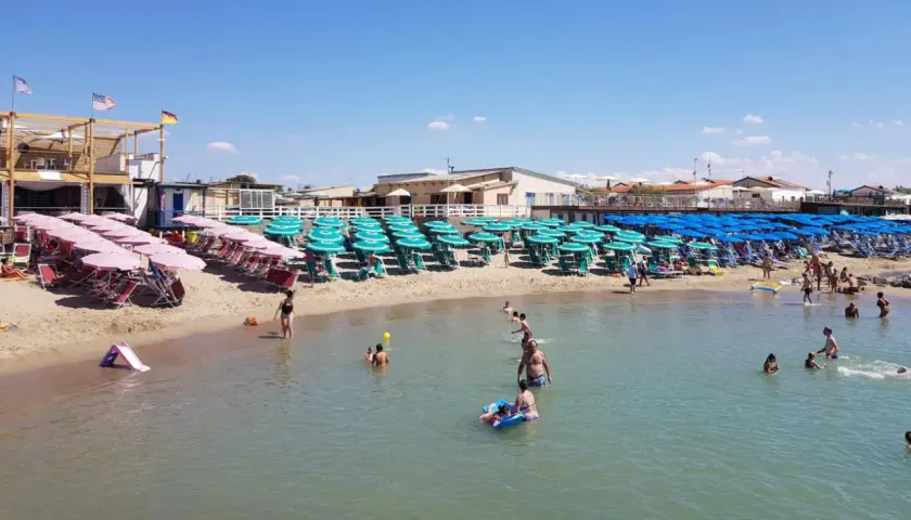 Plage de Marina di Pisa animée, avec des rangées de parasols et de chaises longues sur le sable, et des baigneurs profitant de l'eau claire sous un ciel bleu.