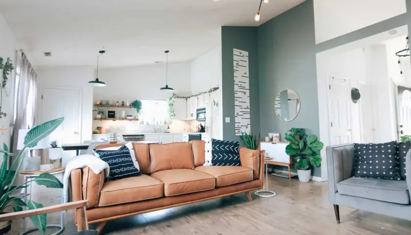Skórzana kanapa w ciepłym odcieniu, szara sofa i zielone rośliny tworzą najlepsze połączenia kolorów w tym przytulnym salonie.