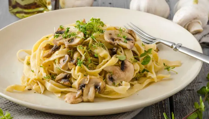 Deliciosa pasta con champiñones frescos y hierbas aromáticas, servida en un plato cremoso.