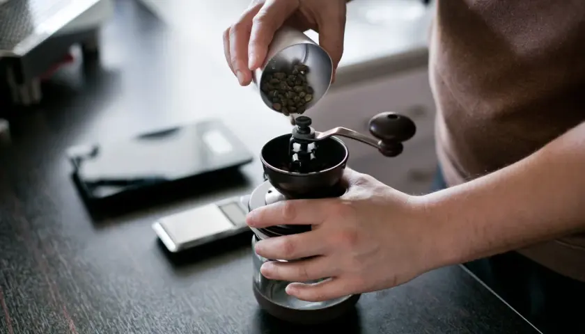 Mani versano chicchi di caffè in un macinino manuale, iniziando la macinazione per un caffè perfetto.
