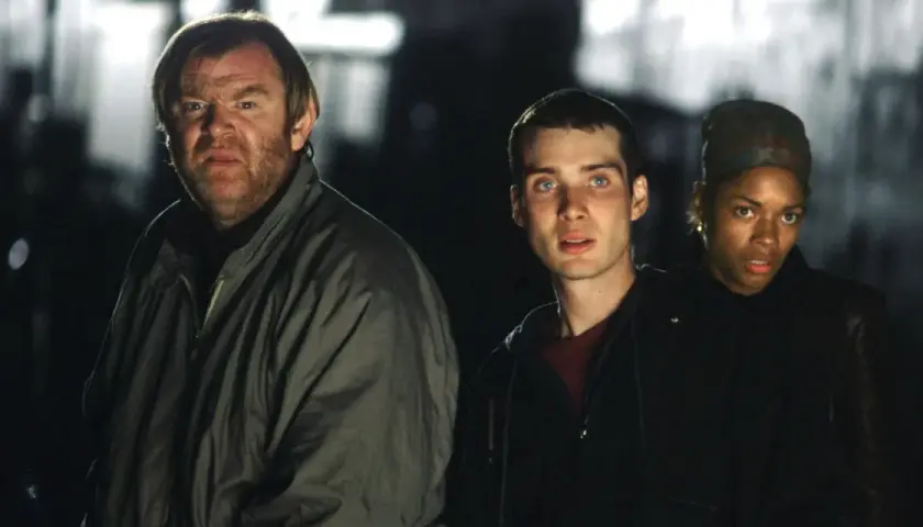 Trzech ocalałych, w tym mężczyzna z groźną miną, przemierzają mroczne ulice w świecie po apokalipsie. To scena z filmu "28 dni później".