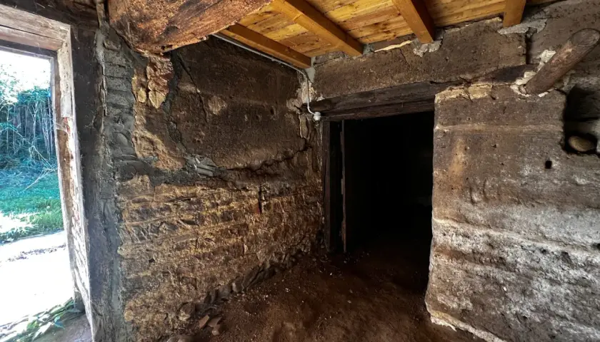 Intérieur d'une maison en pisé en ruine, murs érodés, poutres apparentes. Danger de délabrement.