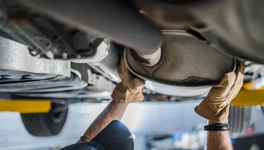 Mani guantate lavorano sul sistema di scarico, forse sostituendo il catalizzatore auto.