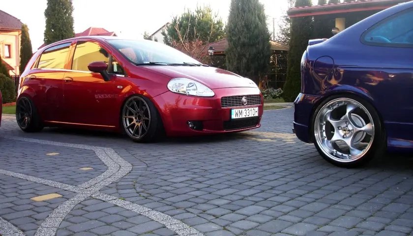 Czerwony Fiat Grande Punto 1.4 z przyciemnianymi szybami i sportowymi felgami, obok niebieski samochód. Rozmiar opon dopasowany do modyfikacji.
