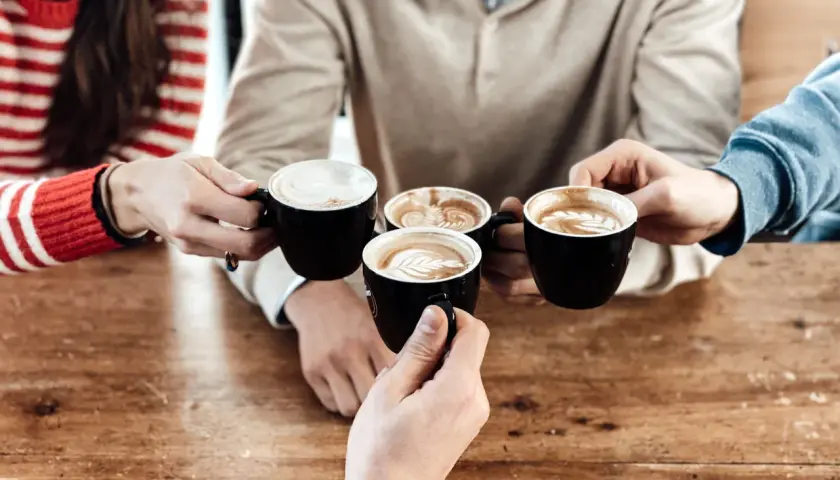 Amici brindano con diversi tipi di caffè al bar, con schiuma artistica e latte macchiato.
