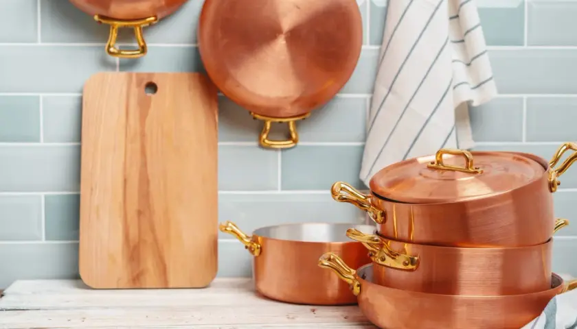 Utensilios de cobre apilados y colgados, junto a una tabla de cortar. Aprende como limpiar cobre para que brillen así.