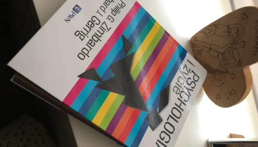 Na biurku leży książka "Psychologia" autorstwa Philipa G. Zimbardo i Richarda J. Gerriga, obok drewniane serce z rysunkami.