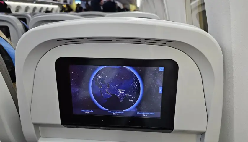 Wnętrze samolotu Neos Air. Ekran pokładowy pokazuje mapę świata z zaznaczoną trasą lotu z Wiednia do Phuket.