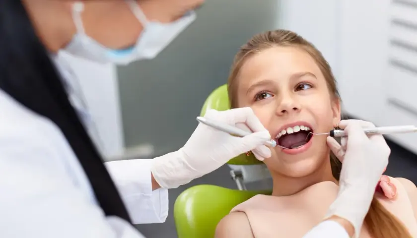 Dziecko u dentysty, które czeka na znieczulenie. Stomatolog w rękawiczkach bada ząb dziewczynki.