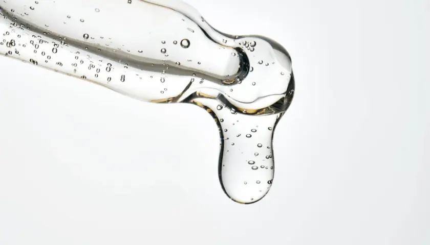 Kropla przejrzystego serum z pęcherzykami powietrza, zawierającego kwasy LHA, spływa z pipety.