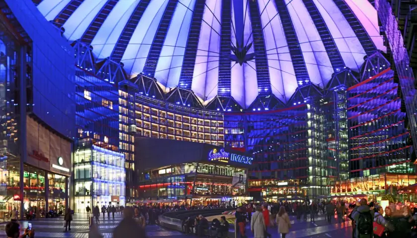 Nocny widok na Sony Center w Berlinie, z oświetlonym dachem i fasadami budynków, pełen ludzi spacerujących po placu.