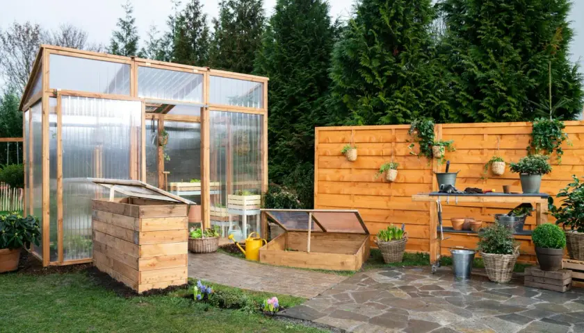 Ein Garten mit einem selbstgebauten Tomatenhaus, Frühbeet und einer Werkbank. Perfekt für alle, die ihr Tomatenhaus selber bauen möchten.