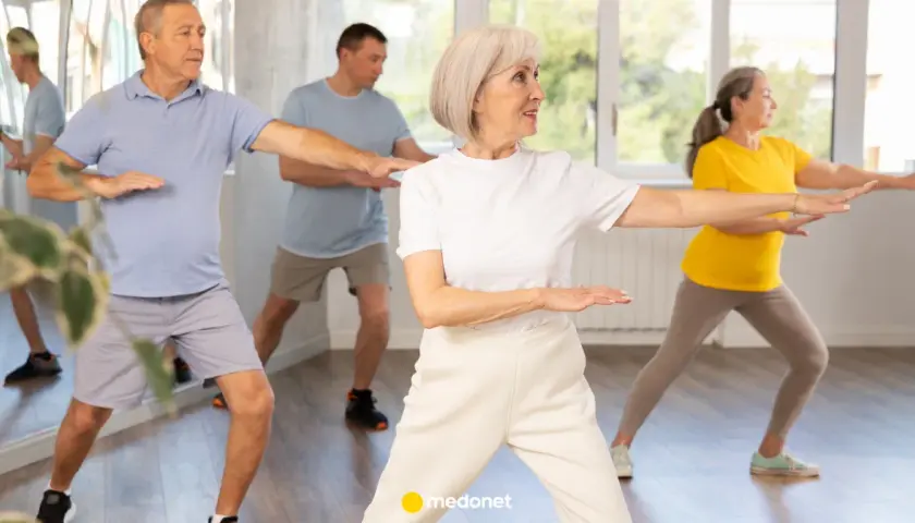 Seniorzy ćwiczą tai chi na krześle, synchronizując ruchy ramion.