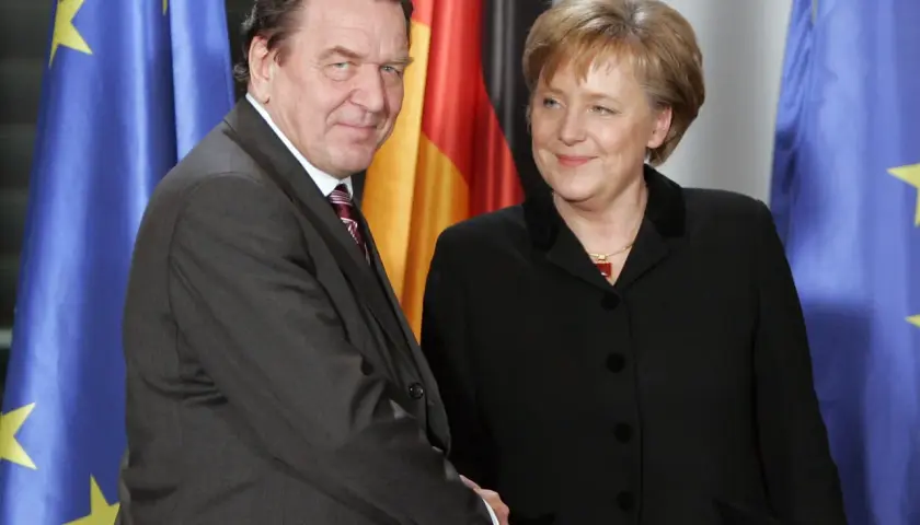 Gerhard Schröder und Angela Merkel, die erste Bundeskanzlerin Deutschlands, vor Flaggen.