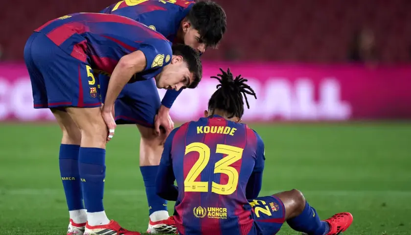 Piłkarze FC Barcelona zmartwieni po kontuzji kolegi. Koundé siedzi na murawie, koledzy pochylają się nad nim.