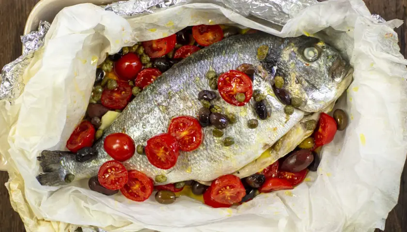 Orata al cartoccio con pomodorini, olive e capperi, un piatto profumato e saporito pronto per essere gustato.