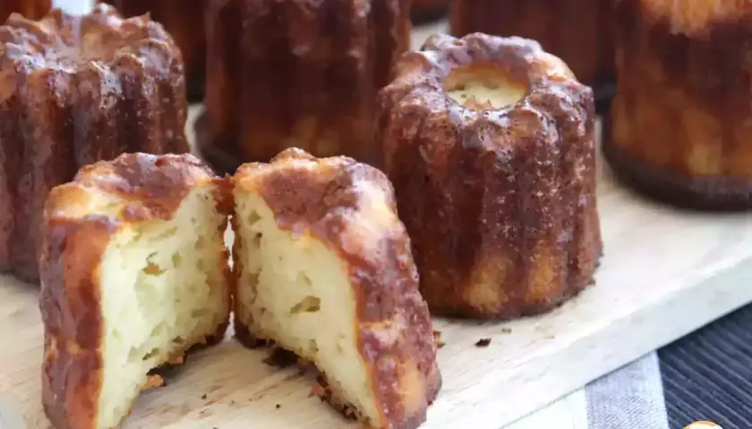 Délicieux cannelés dorés, un classique de la recette cannelés. L'un est coupé en deux, révélant sa mie moelleuse.