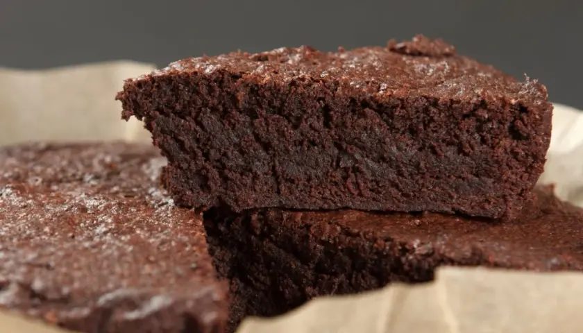Wilgotne brownie bez jajek, posypane cukrem pudrem, ułożone na papierze do pieczenia.