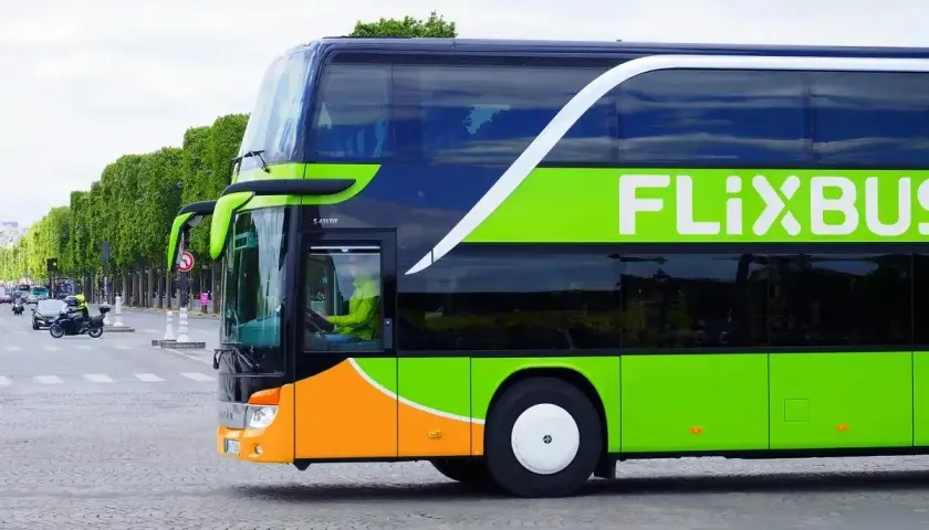 Zielony autokar FlixBus jedzie ulicą. Kierowca w żółtej kurtce prowadzi pojazd. Czy FlixBus robi postoje? Tak, ten autokar na pewno zatrzymuje się na trasie.