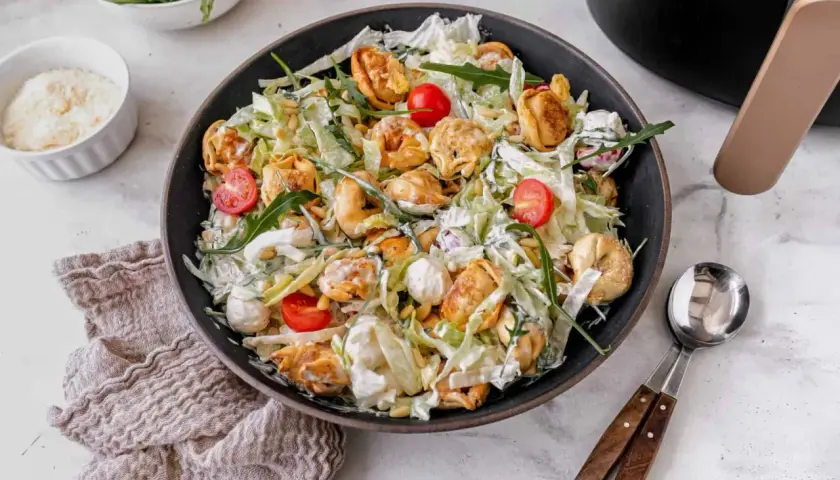 Ein üppiger italienischer Salat mit Tortellini, Kirschtomaten, Rucola und Pinienkernen, übergossen mit einer cremigen Sauce.