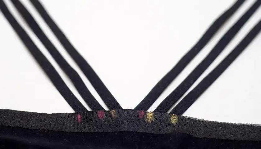 Close-up of three black bra straps crisscrossing over a black fabric band with pink and gold marks.