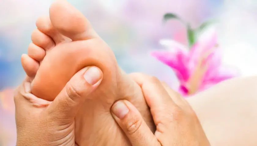 Close-up of hands massaging a foot with a blurred pink flower in the background.